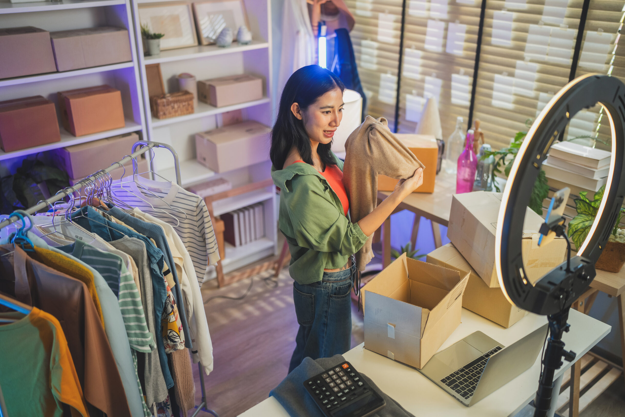 Woman live streaming clothing products using a camera and ring light for online retail.