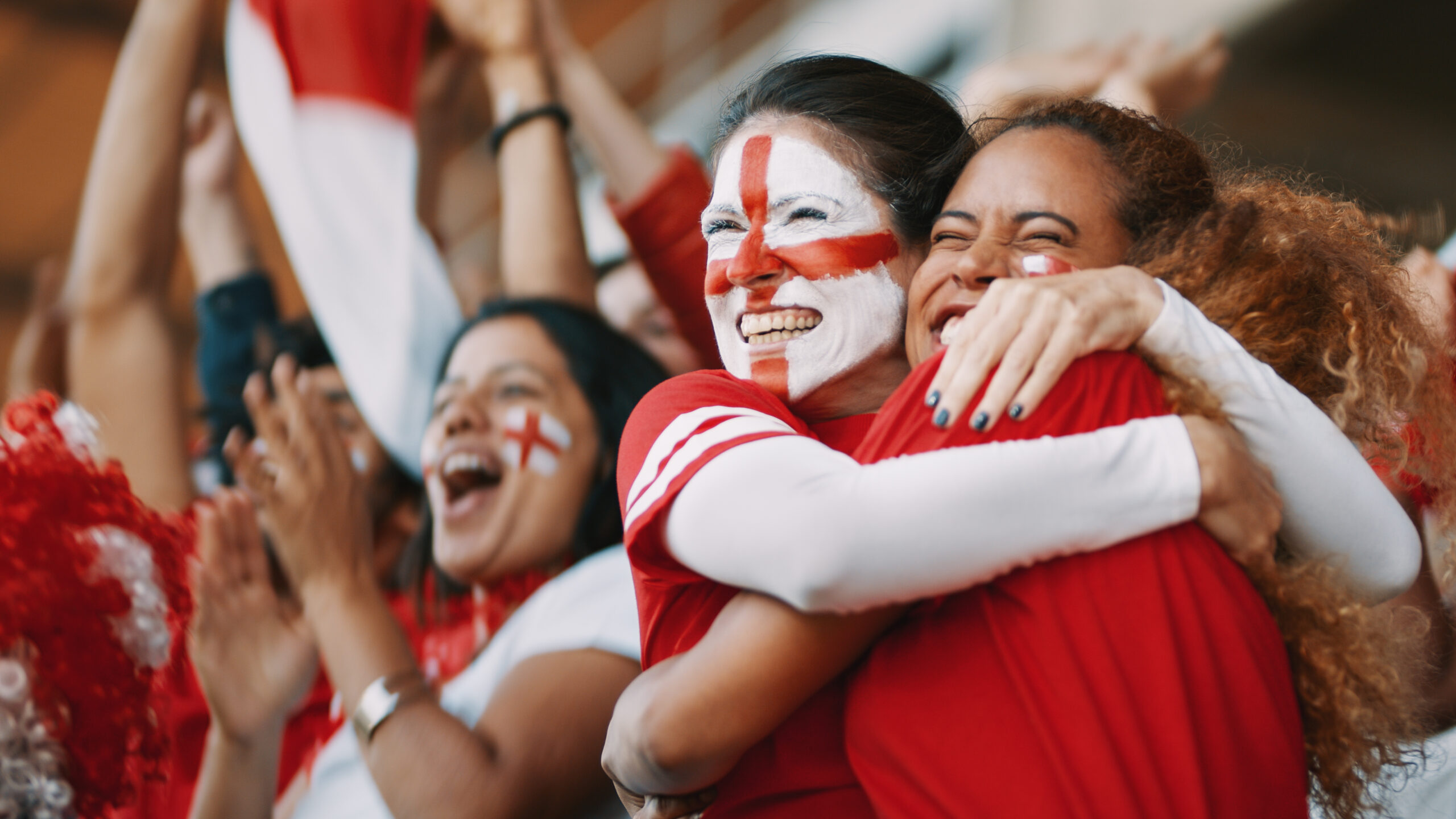 England football supporters celebrating together in a stadium, with one fan wearing a St George's Cross face paint.